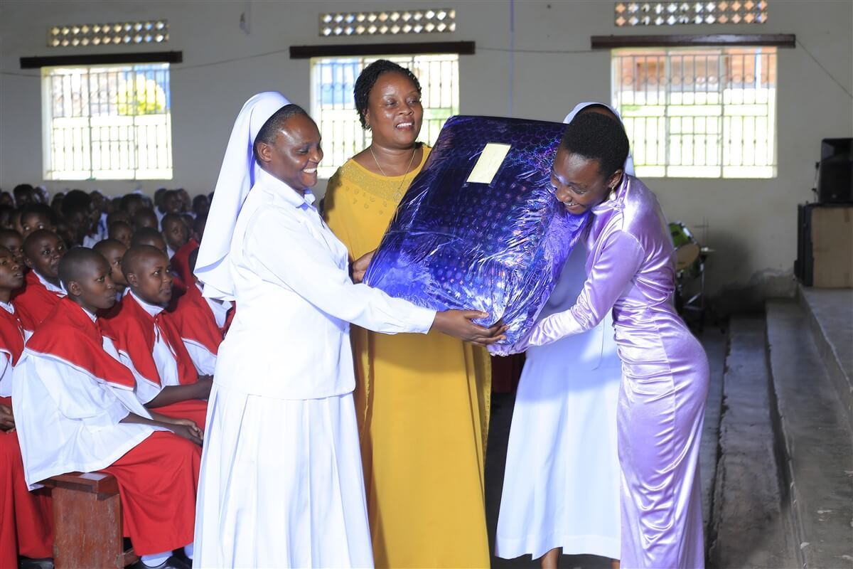 A sister and a teacher hand a large prize wrapped in blue to a student at prize-giving